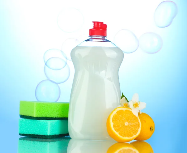 Жидкость для мытья посуды с губками и лимон с цветами на синем фоне — стоковое фото