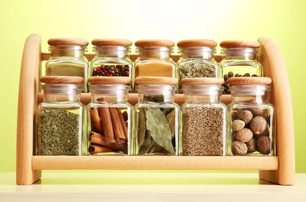 Pulver kryddor i glasburkar på trähylla på grön bakgrund — Stockfoto