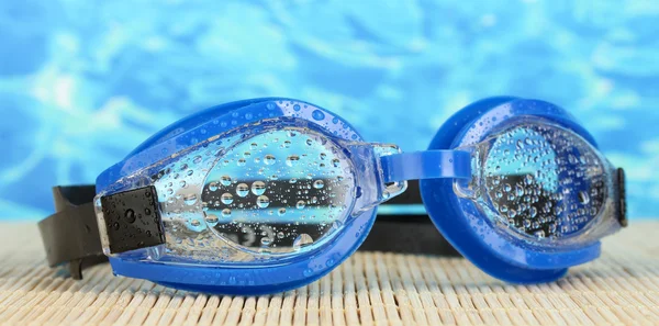 Occhiali da bagno blu con gocce su un cuscinetto di bambù, su fondo blu mare — Foto Stock