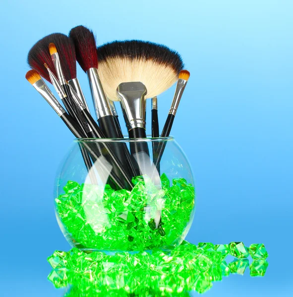 Pincéis de maquiagem em uma tigela com pedras no fundo azul — Fotografia de Stock