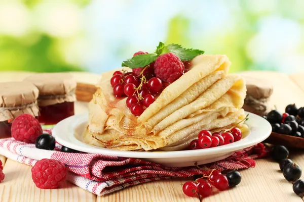 Pancakes with berries, jam and honey on wooden table on green background — Stock Photo, Image