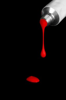 Red paint follows from the tube on black background close-up clipart