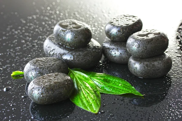 Spa stenen met druppels en groene bladeren op grijze achtergrond — Stockfoto