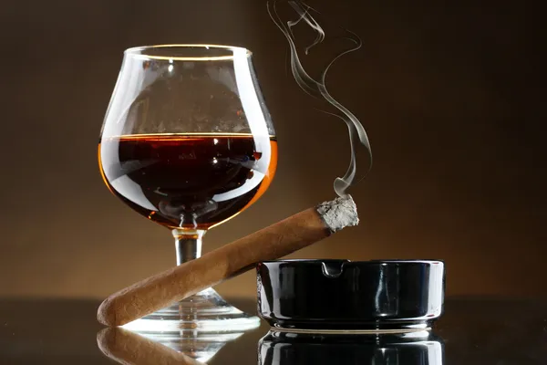 Vaso de brandy y cigarro sobre fondo marrón — Foto de Stock
