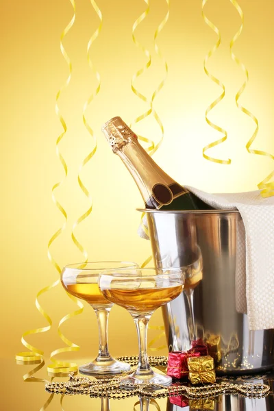 黄色の背景にシャンパンのグラスと氷バケットのシャンパンのボトル — ストック写真
