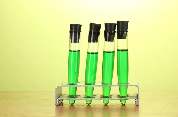 Tubes à essai avec liquide vert sur table en bois sur fond vert — Photo