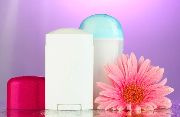 Botellas de desodorante con flor sobre fondo púrpura —  Fotos de Stock