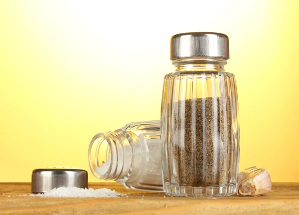 Sól i pieprz mills, na drewnianym stole na żółtym tle — Zdjęcie stockowe