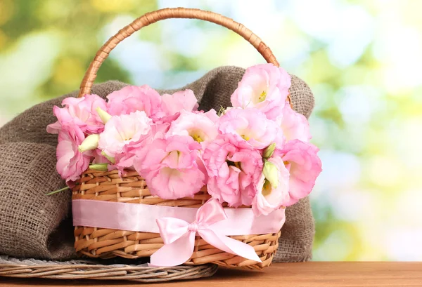 Strauß Eustoma-Blumen im Korb, auf Holztisch, auf grünem Hintergrund — Stockfoto