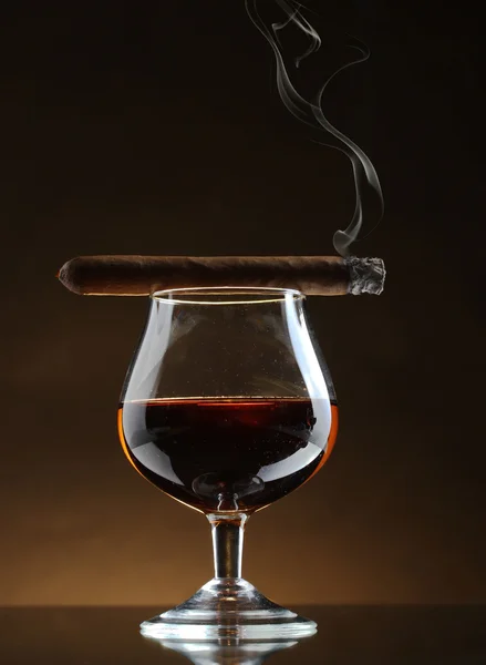 Glass of brandy and cigar on brown background — Stock Photo, Image