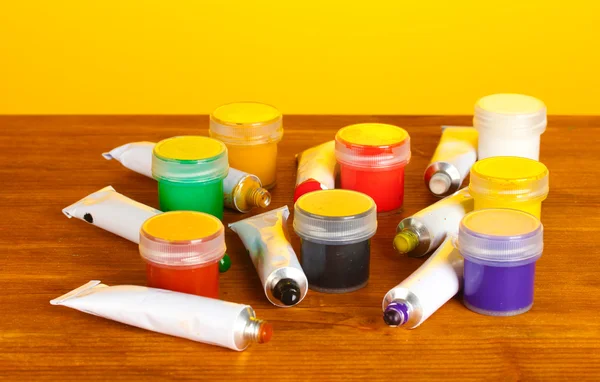 Tubes with colorful watercolors and jars with gouache on wooden table on bright yellow background — Stock Photo, Image