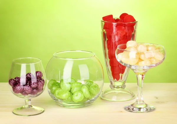 Farbbonbons in Gläsern auf Holztisch auf grünem Hintergrund — Stockfoto