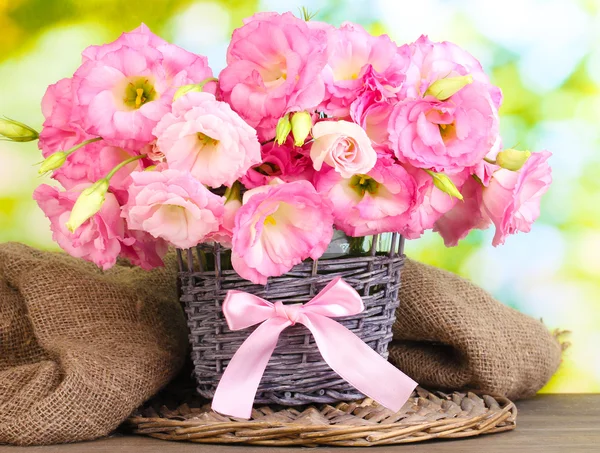 Букет квітів еустоми у плетеній вазі, на дерев'яному столі, на зеленому фоні — стокове фото