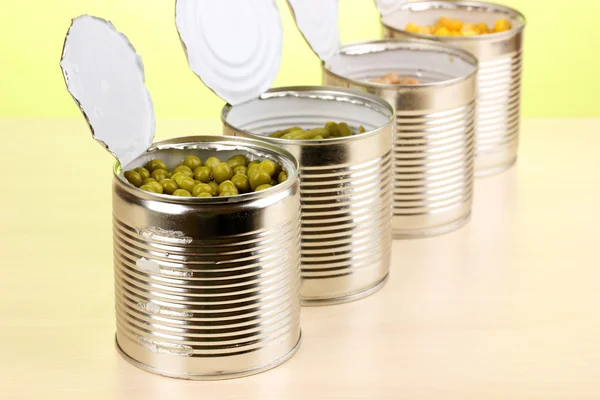 Offene Blechdosen mit Erbsen, Mais, Bohne und französischer Bohne auf Holztisch auf grünem Hintergrund — Stockfoto