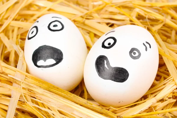 Белые яйца со смешными лицами в соломе — стоковое фото