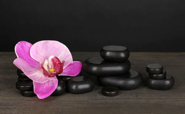 Wellness-Steine mit Orchideenblume auf Holztisch auf grauem Hintergrund — Stockfoto