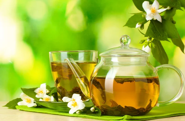 Groene thee met jasmijn in cup en theepot op houten tafel op groene achtergrond — Stockfoto