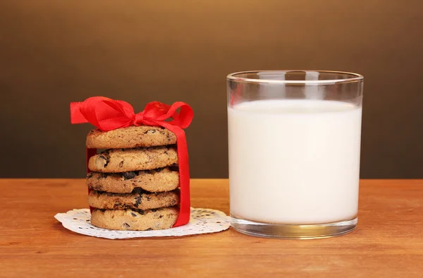 Bicchiere di latte e biscotti su tavolo di legno su sfondo marrone — Foto Stock