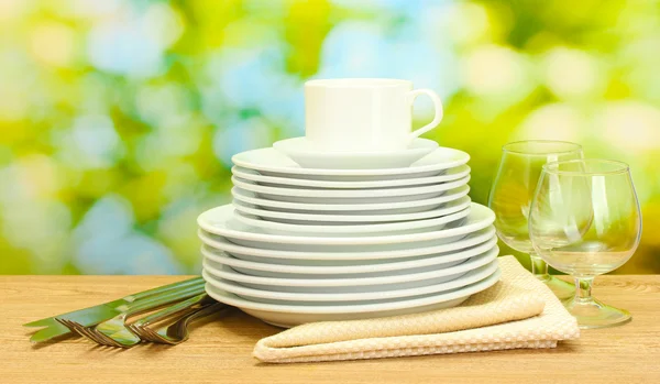 Platos limpios vacíos, vasos y taza en la mesa de madera sobre fondo verde —  Fotos de Stock