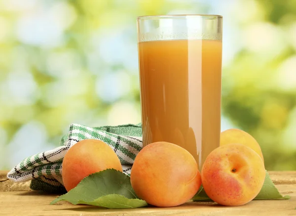 Glass of apricot juice and fresh apricots on wooden table on green background — Stock Photo, Image