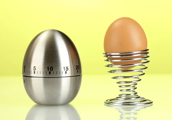 Χρονόμετρο αυγό και το αυγό σε μέταλλο σταθεί σε πράσινο φόντο — Φωτογραφία Αρχείου