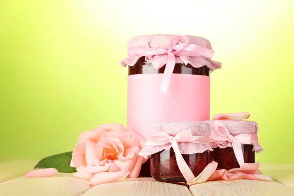 Frascos con mermelada de rosa y flor sobre mesa de madera sobre fondo verde — Foto de Stock