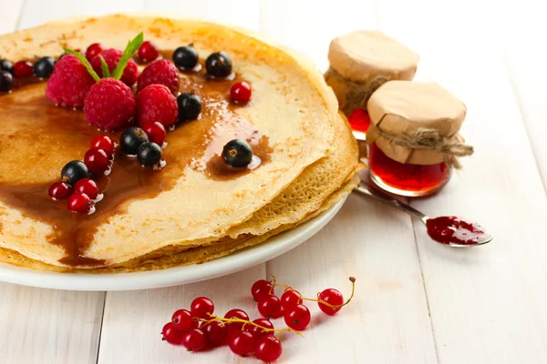Вкусные блинчики с ягодами и джемом на тарелке на деревянном столе — стоковое фото
