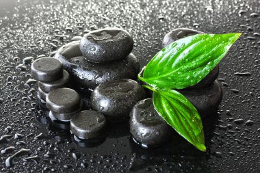 Spa stones with drops and green leaves on grey background clipart