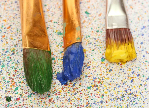 Brushes with colorful paint on colorful splashes background close-up — Stock Photo, Image