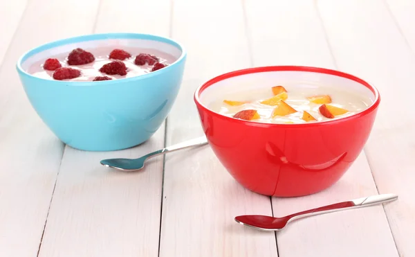 Йогурт с персиками и малиной в мисках на деревянном фоне — стоковое фото