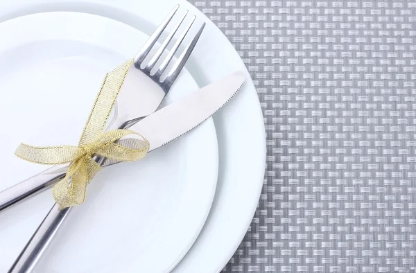 Assiettes blanches vides avec fourchette et couteau attachées avec un ruban sur une nappe grise — Photo