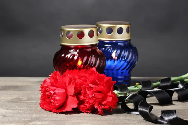 Ліхтар пам'яті зі свічками, червоними гвоздиками та стрічкою на дерев'яному столі на сірому фоні — стокове фото