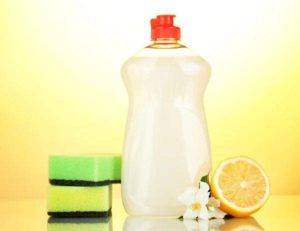 Líquido lavavajillas con esponjas y limón con flores sobre fondo amarillo — Foto de Stock