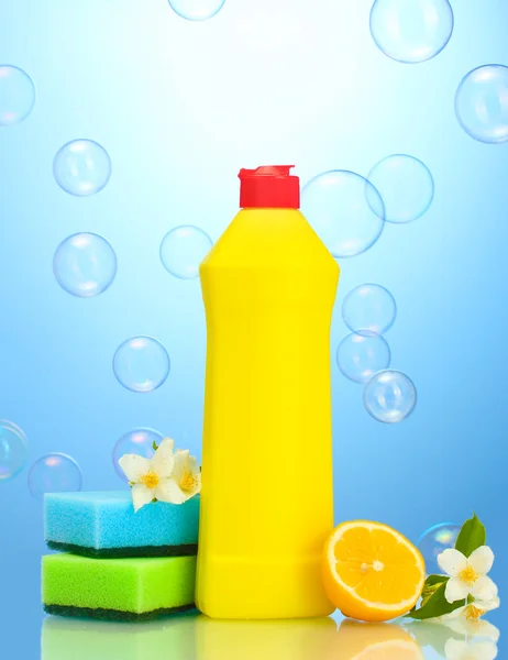 Líquido lavavajillas con esponjas y limón con flores sobre fondo azul — Foto de Stock