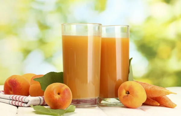 Glasögon med morot och aprikos juice på vita träbord på grön bakgrund — Stockfoto
