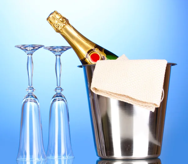 Champagne bottle in bucket with ice and glasses on blue background — Stock Photo, Image