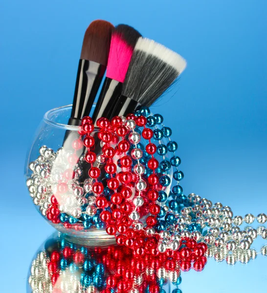 Make-up štětce v misce s perlový náhrdelník na modrém pozadí — Stock fotografie