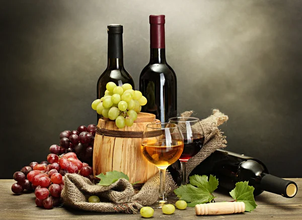 Barril, botellas y copas de vino y uvas maduras sobre mesa de madera sobre fondo gris Imágenes De Stock Sin Royalties Gratis