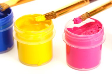 Brushes on the jars with colorful gouache on white background close-up