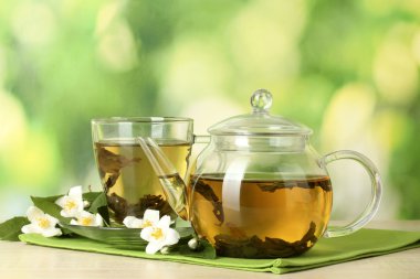 Green tea with jasmine in cup and teapot on wooden table on green background