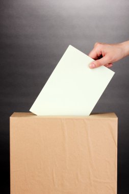 Hand with voting ballot and box on grey background clipart