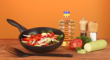 Frying pan with vegetables on red background clipart