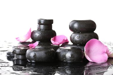 Spa stones with drops and rose petals on white background