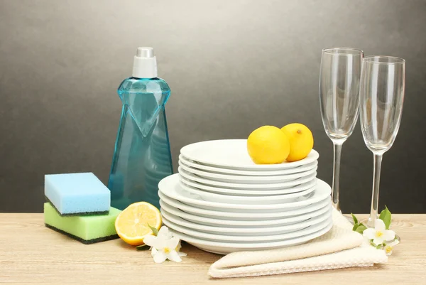 Lege schoon platen en bril met afwasmiddel, sponzen en citroen op houten tafel op grijze achtergrond — Stockfoto