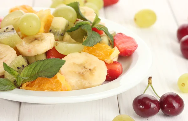 Insalata di frutta fresca su piatto e bacche su tavolo di legno bianco — Foto Stock