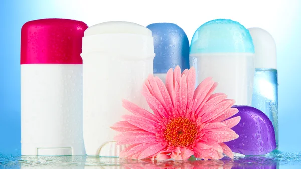 Botellas de desodorante con flor sobre fondo azul — Foto de Stock