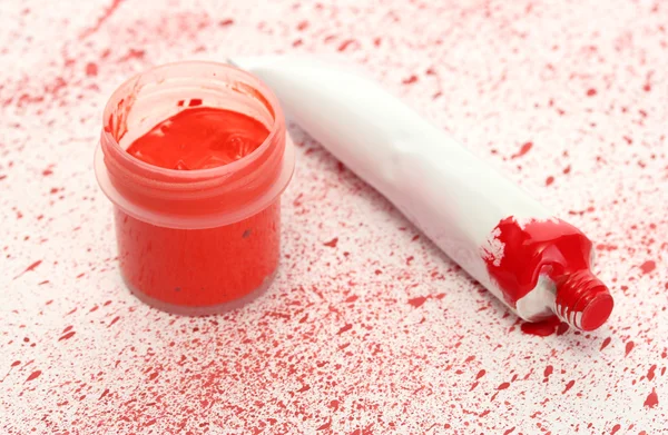 Pot met rode gouache en buis met rode waterverf op achtergrond van rode spray close-up — Stockfoto
