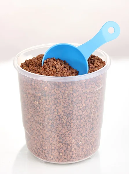 Measuring spoon and plastic container with grain isolated on white — Stock Photo, Image