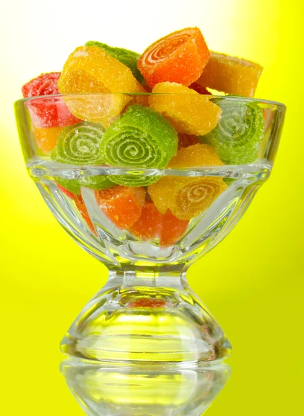 Kleurrijke gelei snoepjes in in glazen kom op groene achtergrond — Stockfoto