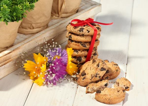 Čokoládu čipy cookies s červenou stužku a květy na dřevěný stůl — Stock fotografie